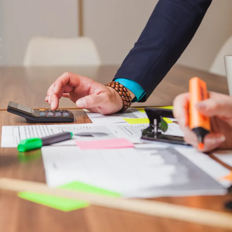 Hands working through tax documents with a calculator and highlighter on a desk